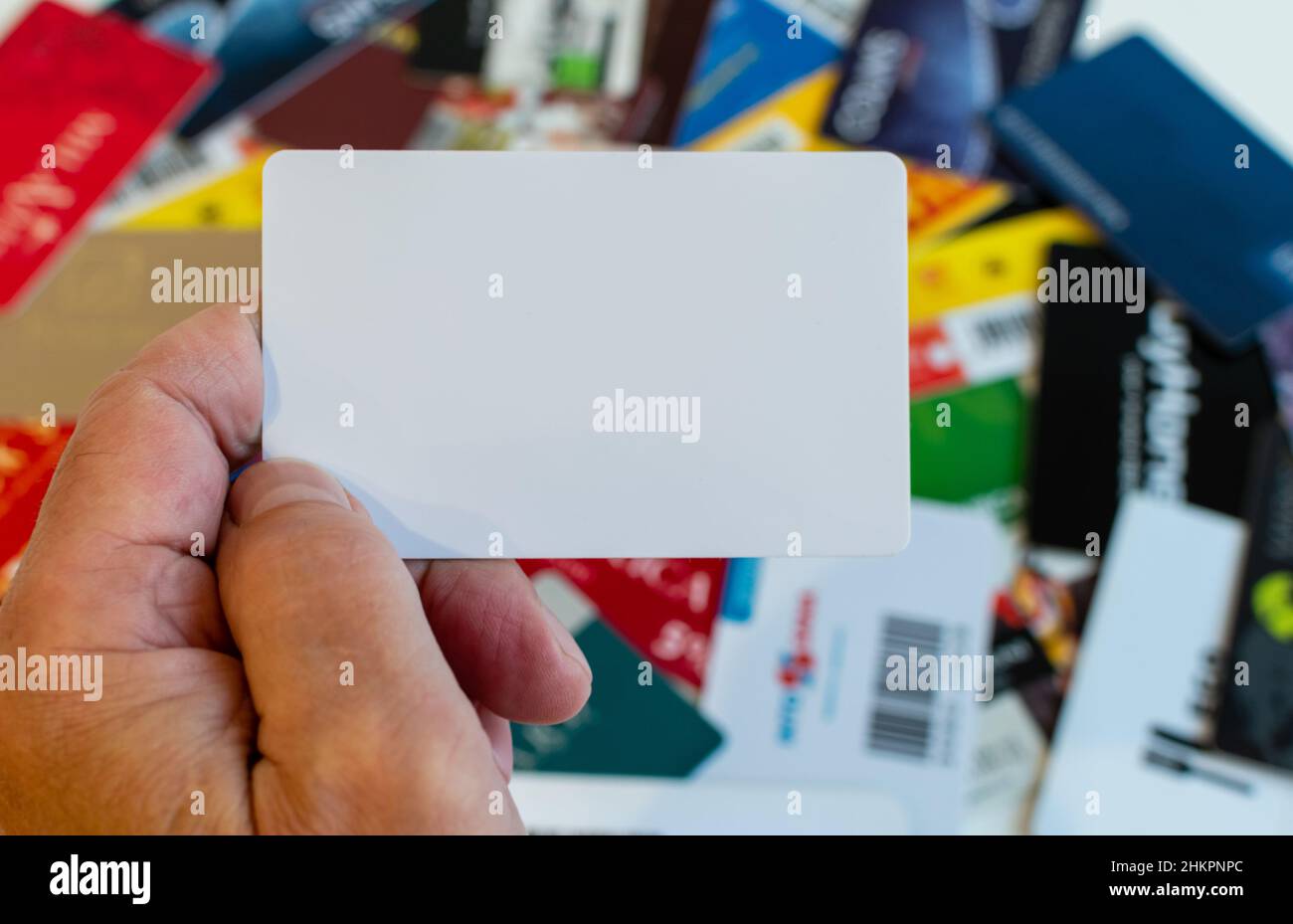 Carta in plastica vuota in mano su sfondo sfocato di varie carte fedeltà in plastica Foto Stock