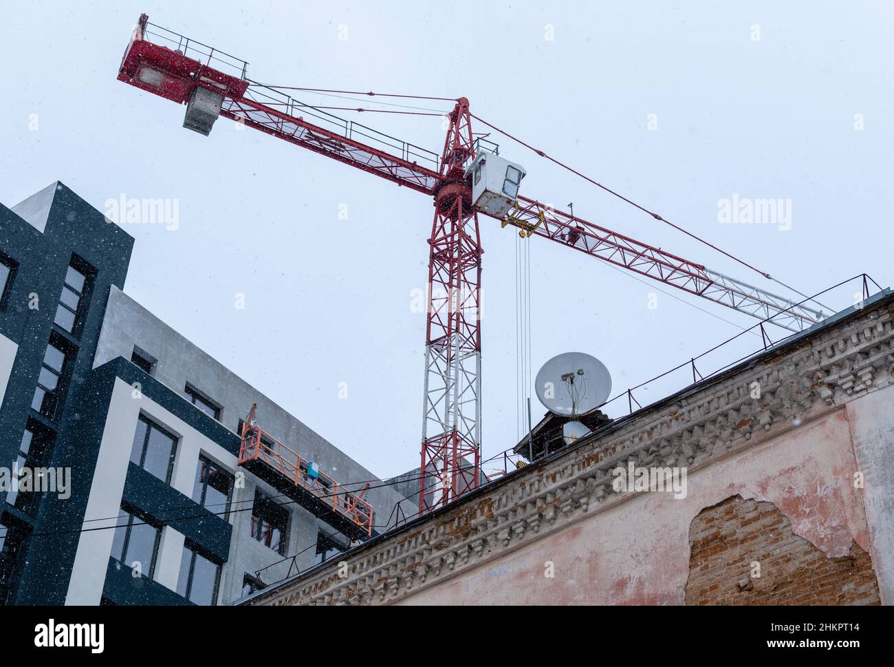 Gru da costruzione su sfondo di vecchie e nuove case e cielo grigio con nevicate leggere Foto Stock