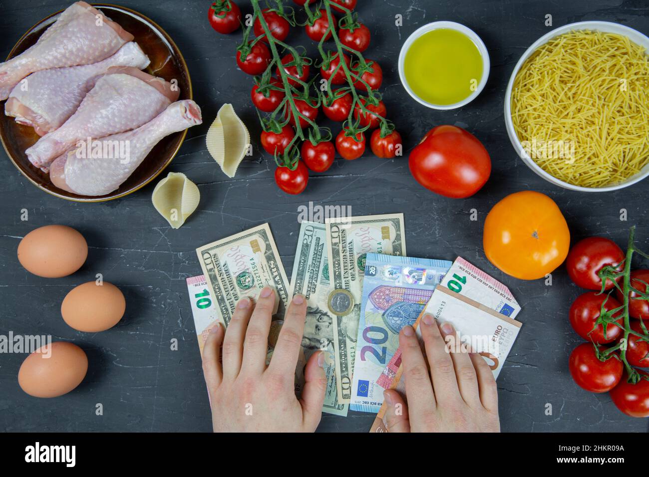Crisi politica e finanziaria, costi elevati, concetto di cibo costoso. Le mani femminili tengono euro e dollaro e cibo quotidiano su sfondo nero. Foto Stock