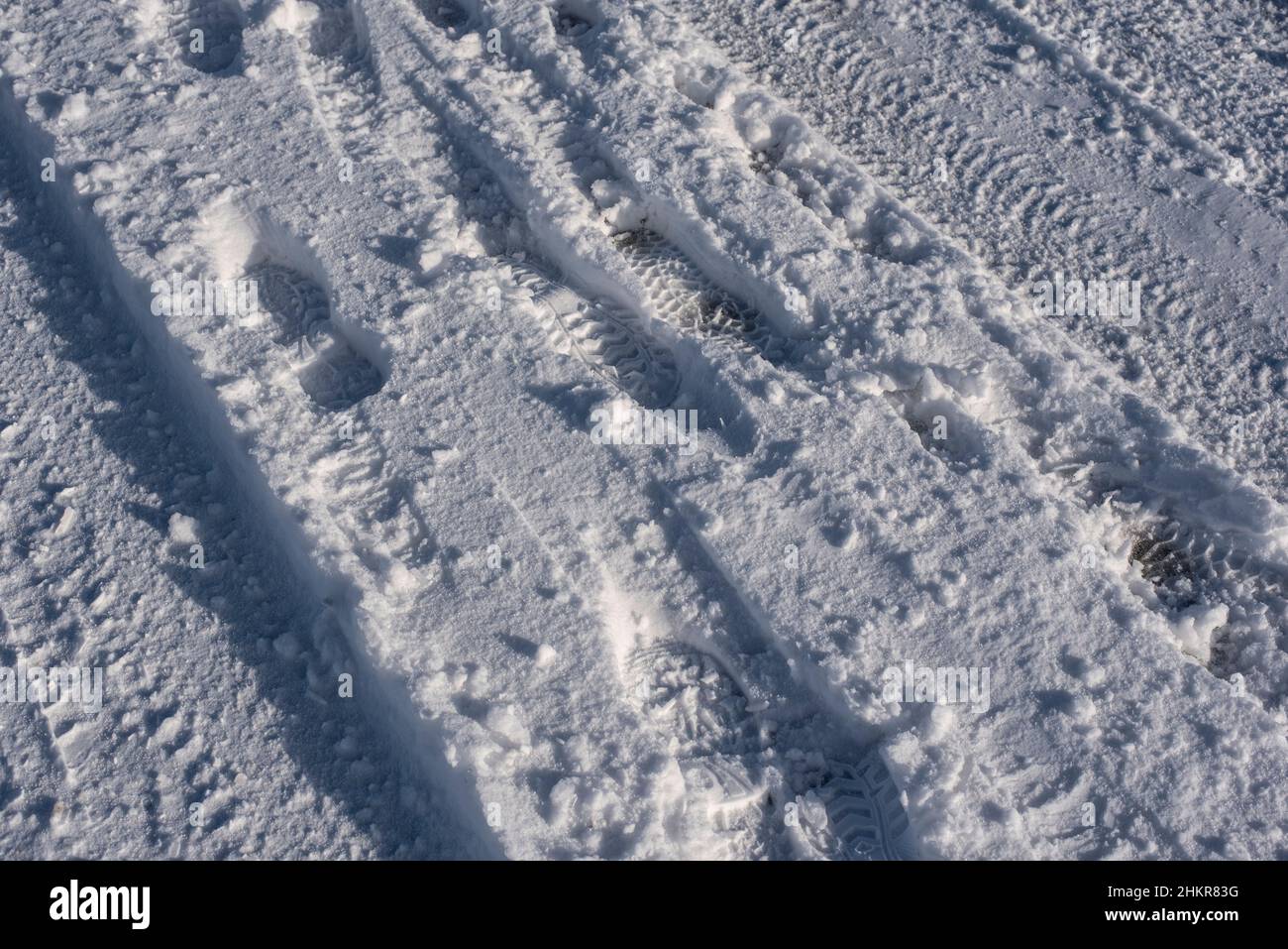 una strada coperta di neve in una giornata invernale soleggiata con impronte e pneumatici Foto Stock