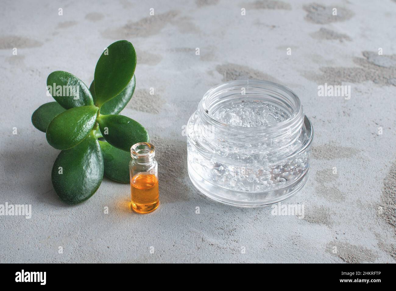 Struttura in gel con bolle di acido ialuronico e rami di aloe vera in un vaso di vetro su sfondo concreto Foto Stock