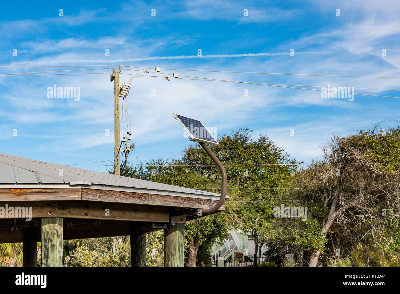 Un piccolo pannello solare fissato al tetto di un padiglione del parco è giustapposto contro un polo elettrico e fili. Foto Stock