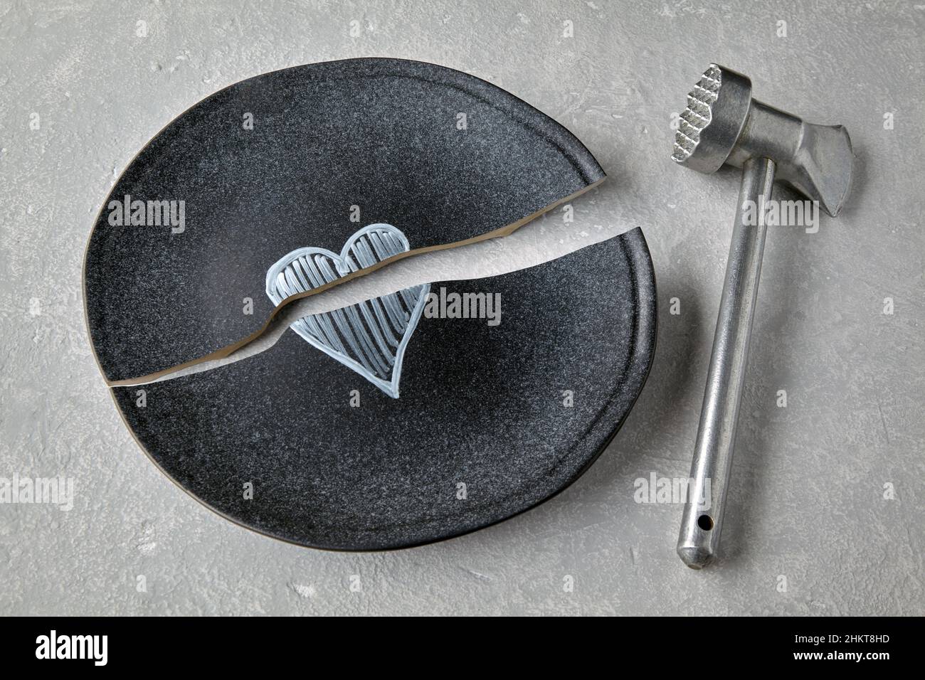 Piastra in ceramica rotta con un cuore dipinto e un martello da cucina Foto Stock