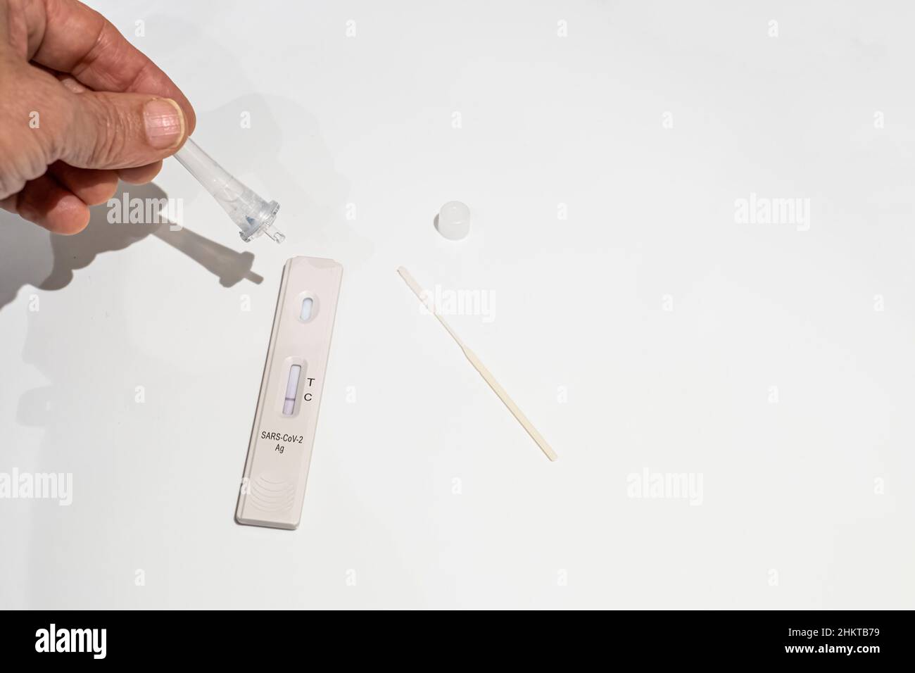 una mano con una goccia di contagocce su un test antigenico per il rilevamento del virus corona, variante omicron, sfondo bianco, fuoco selettivo sul recettore, c Foto Stock