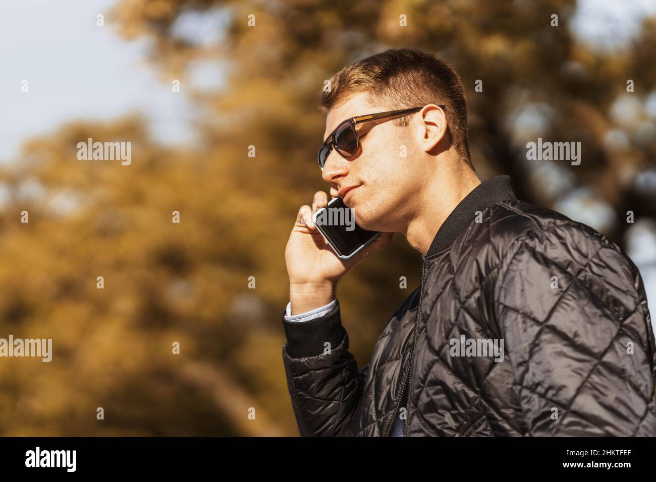 un uomo che indossa occhiali da sole ascolta un messaggio audio sul suo cellulare. Foto Stock