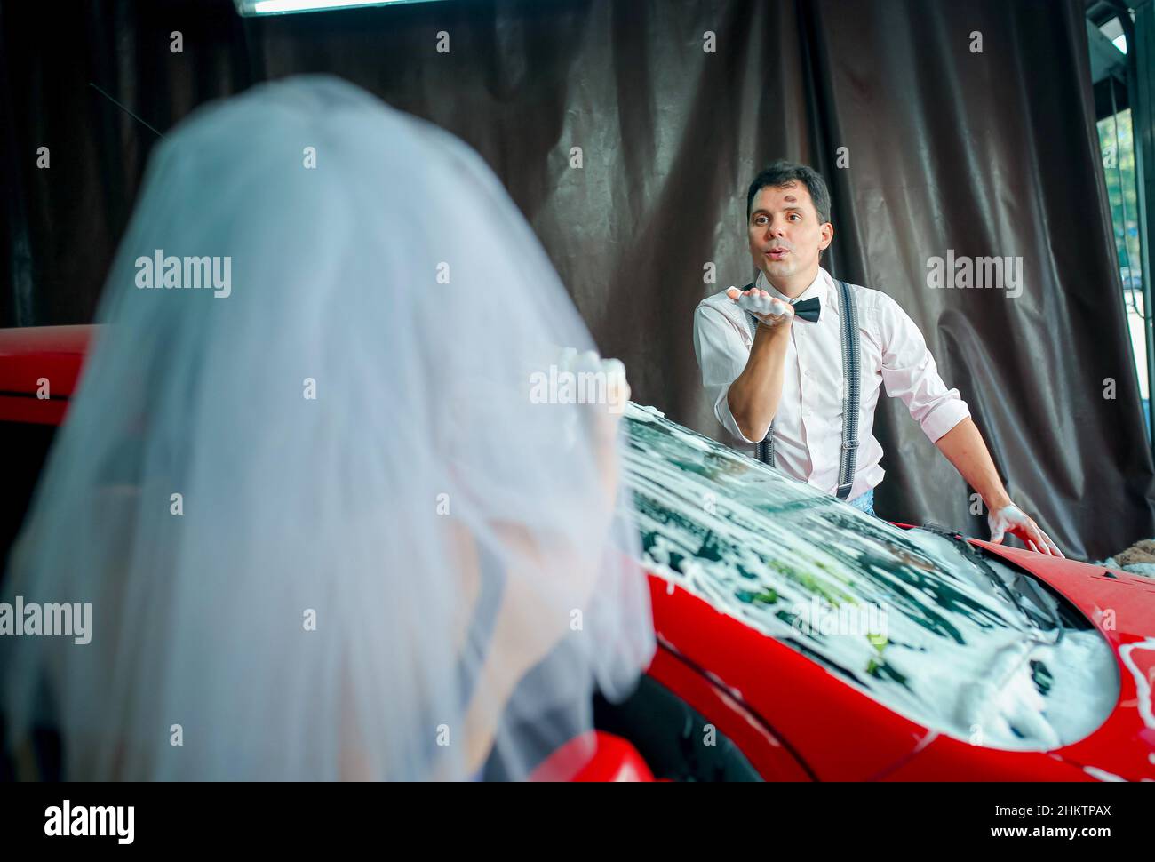 Una donna e un uomo lavano l'automobile nel loro anniversario di nozze. L'uomo soffia un bacio. Foto Stock