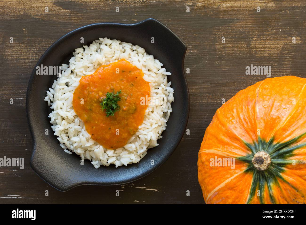 Riso con salsa di zucca su piatto nero su sfondo di legno Foto Stock