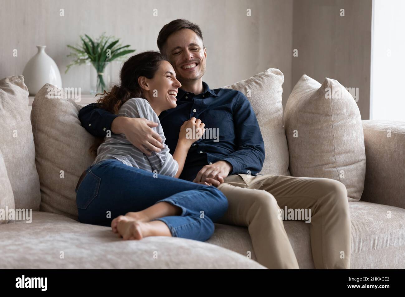 Ridendo la coppia abbracciando, rilassandosi seduti sul divano insieme Foto Stock