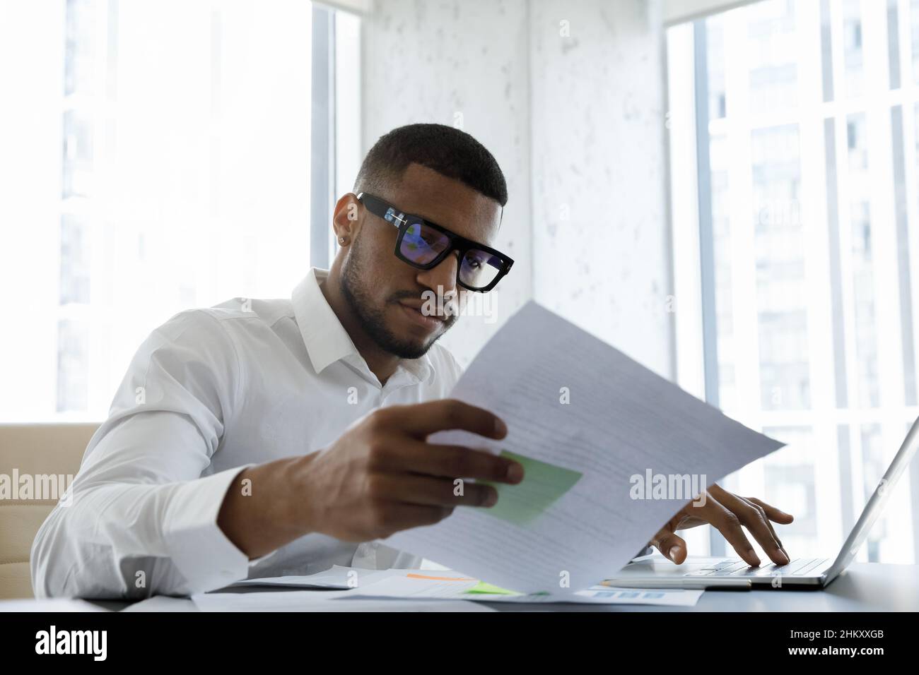 Responsabile africano americano serio in occhiali di stile che legge il documento corporativo Foto Stock