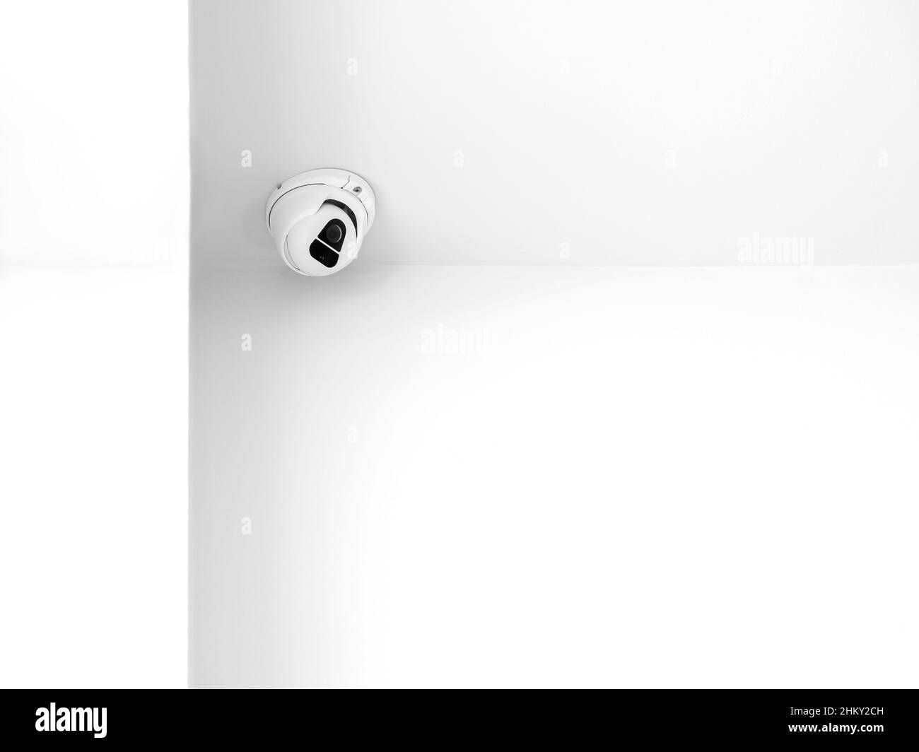 Una telecamera di sorveglianza CCTV per interno bianca che monitora la sicurezza sul soffitto nell'angolo della stanza all'interno dell'edificio bianco e pulito con spazio per le copie. Foto Stock