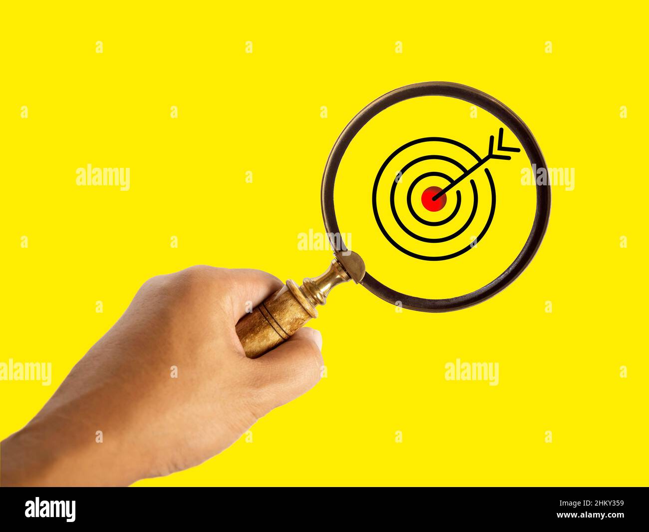 Target board, icona a forma di occhio di bue rossa all'interno della lente d'ingrandimento in mano per il target di business focus su sfondo giallo. Magnifier e dartboard business Foto Stock