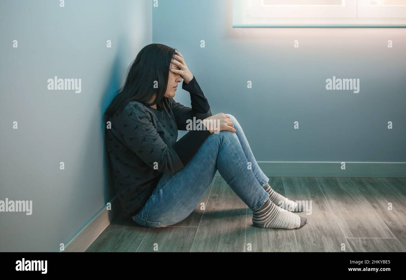 Donna con depressione con mano sul viso seduta sul pavimento Foto Stock