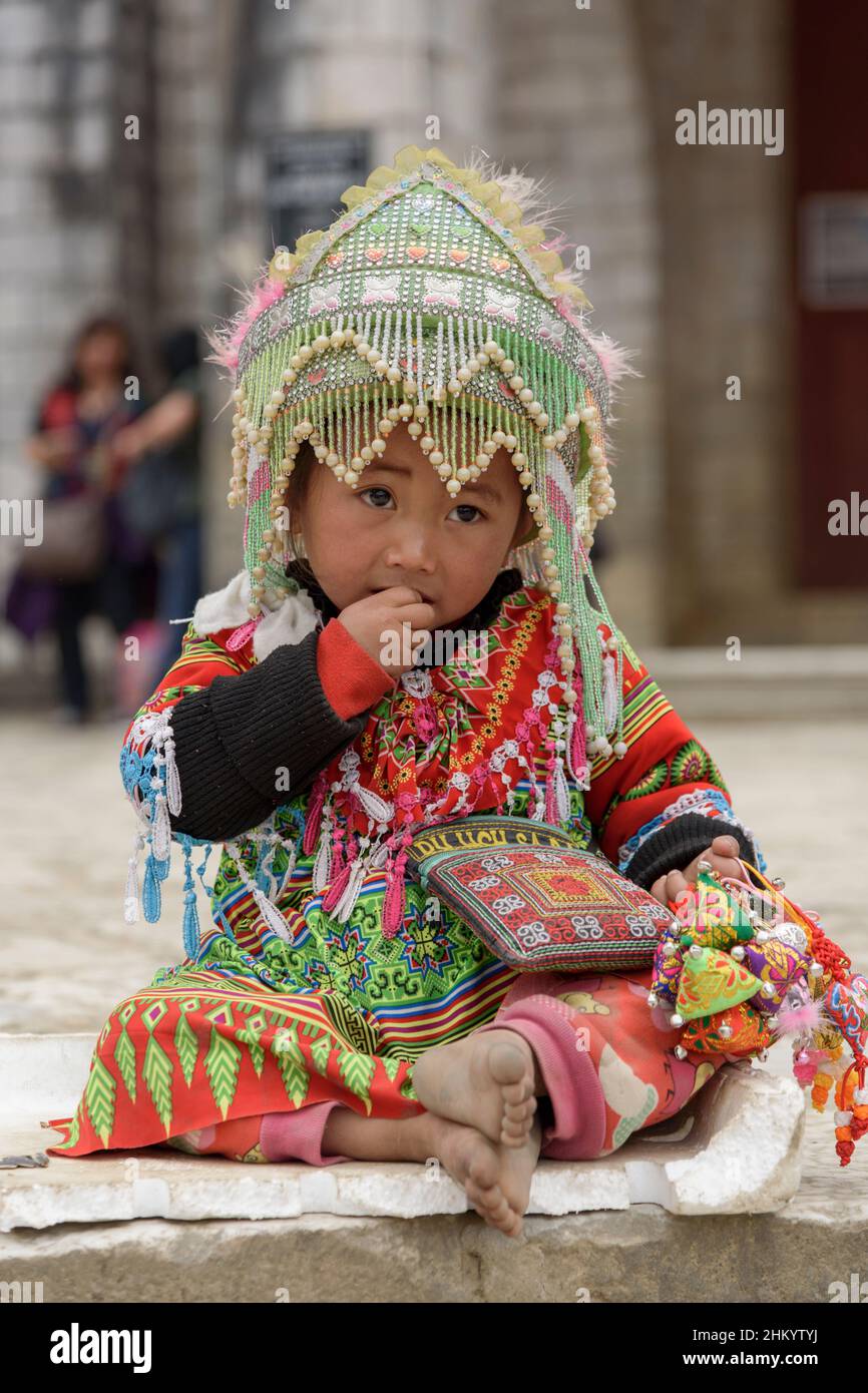Una giovane ragazza, indossando abiti tradizionali della tribù Hmong, aspetta di posare per le fotografie dei turisti nella piazza della città, Sapa (SA Pa), Lao Cai, Vietnam Foto Stock