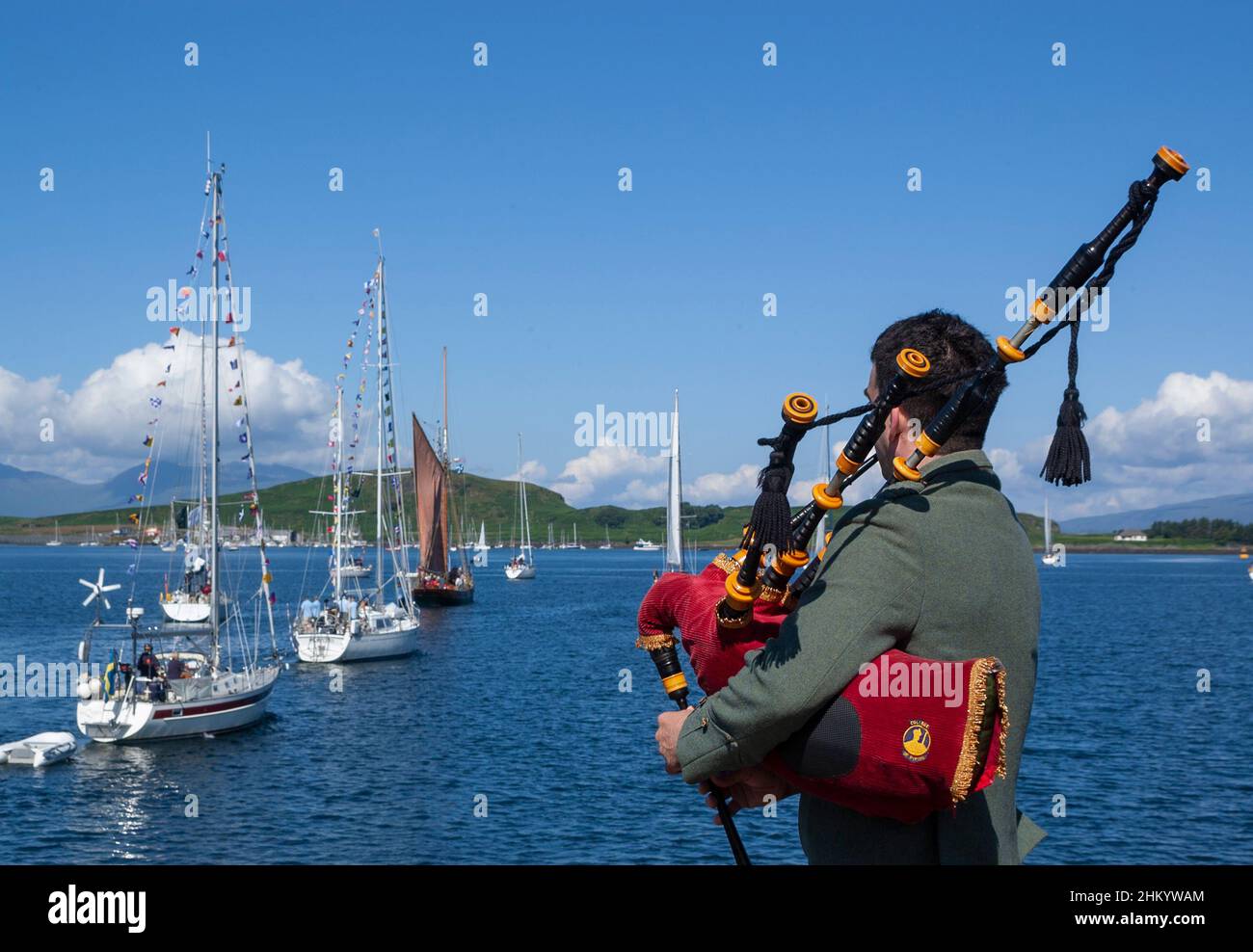 Piper sulla banchina di Oban piping la flotta di barche come lasciare il porto sul rally Malts Classics per visitare varie distillerie di whisky, Scozia Foto Stock