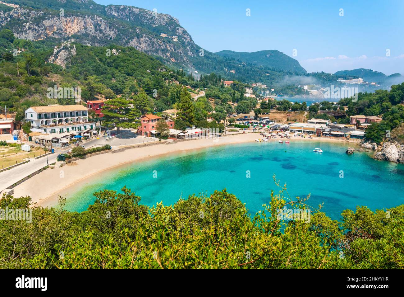 Paleokastritsa spiaggia e villaggio sull'isola di Corfù, Grecia. Spiaggia pittoresca con acque cristalline turchesi, spiaggia di ciottoli Agios Spiridon, montagne Foto Stock