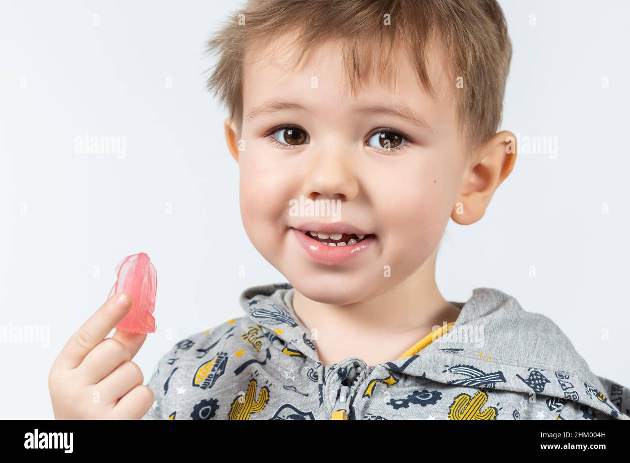 Carino ragazzo caucasico piccolo con capelli biondi sta tenendo un addestratore dentistico miofunzionale rosa su bianco lo sfondo. Tariner dentale è fatto per aiutare uguale Foto Stock