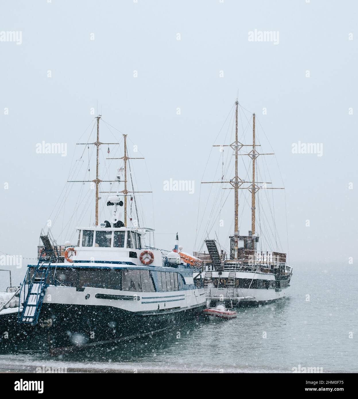 Primo piano delle barche di mare ormeggiate vicino al molo durante una nevicata. Foto Stock