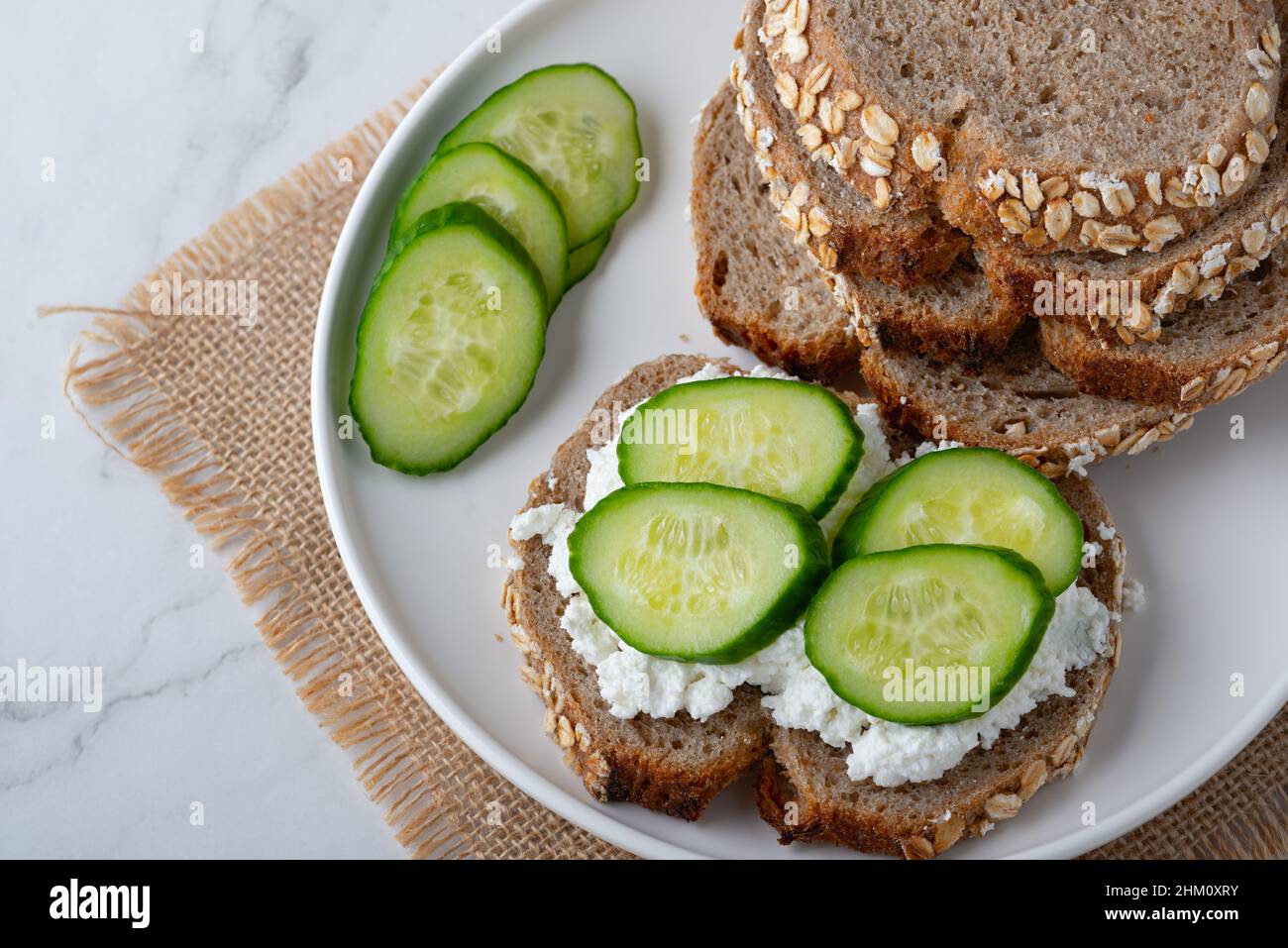 Fette di pane di segale con formaggio casereccio e cetrioli su sfondo bianco Foto Stock