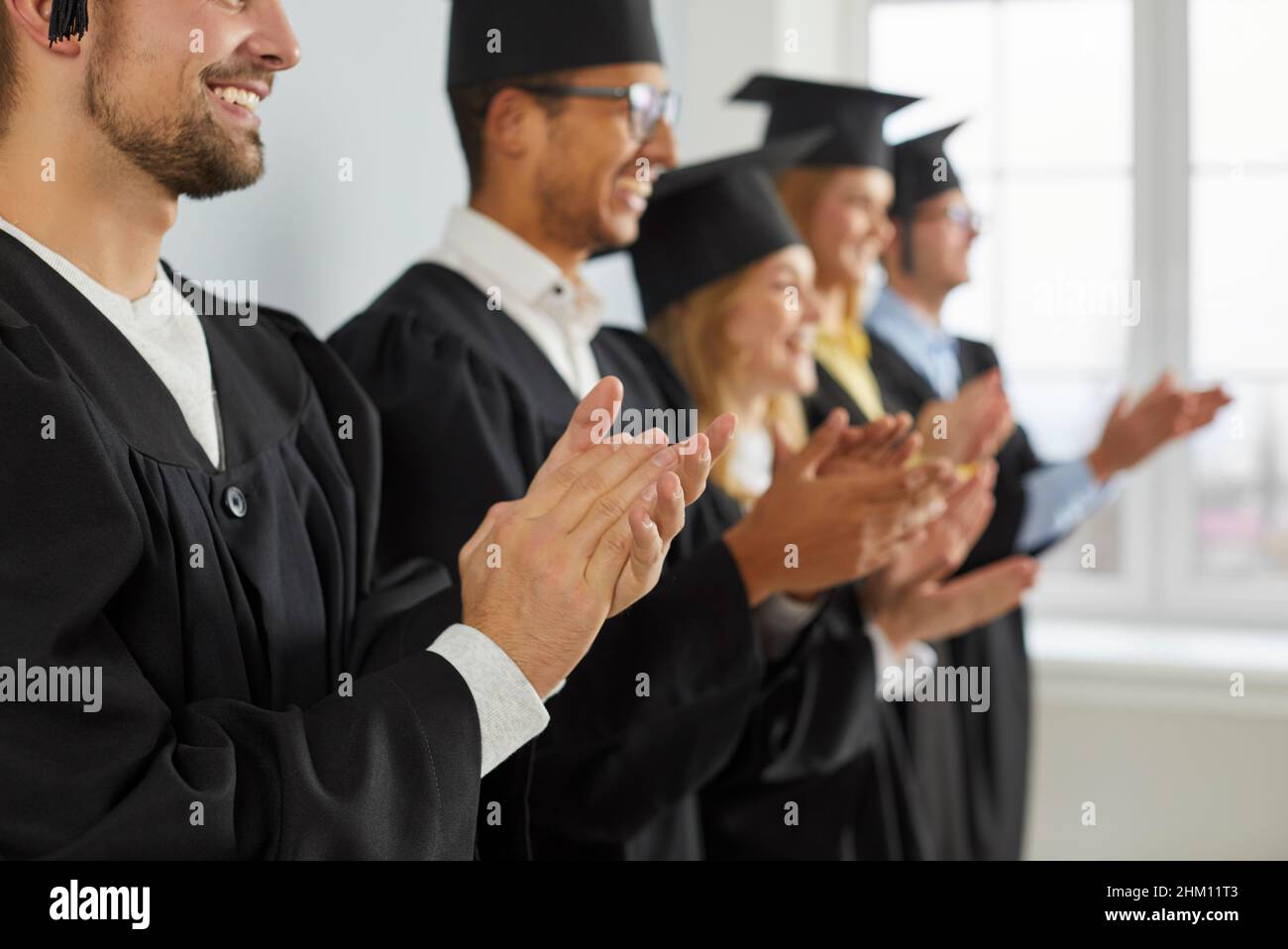 Felice università laureati in cappelli e camici sorridendo e stringendo le mani alla loro laurea Foto Stock