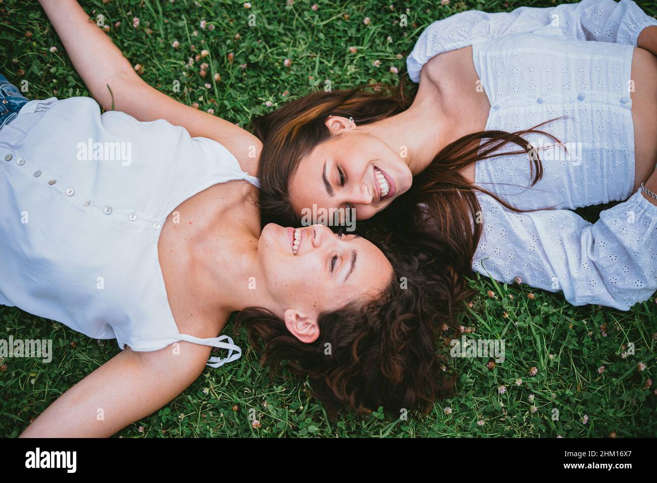 Due ragazze adolescenti sorridendo e guardandosi mentre si stendono sull'erba in un parco. Sembrano rilassati. Foto Stock