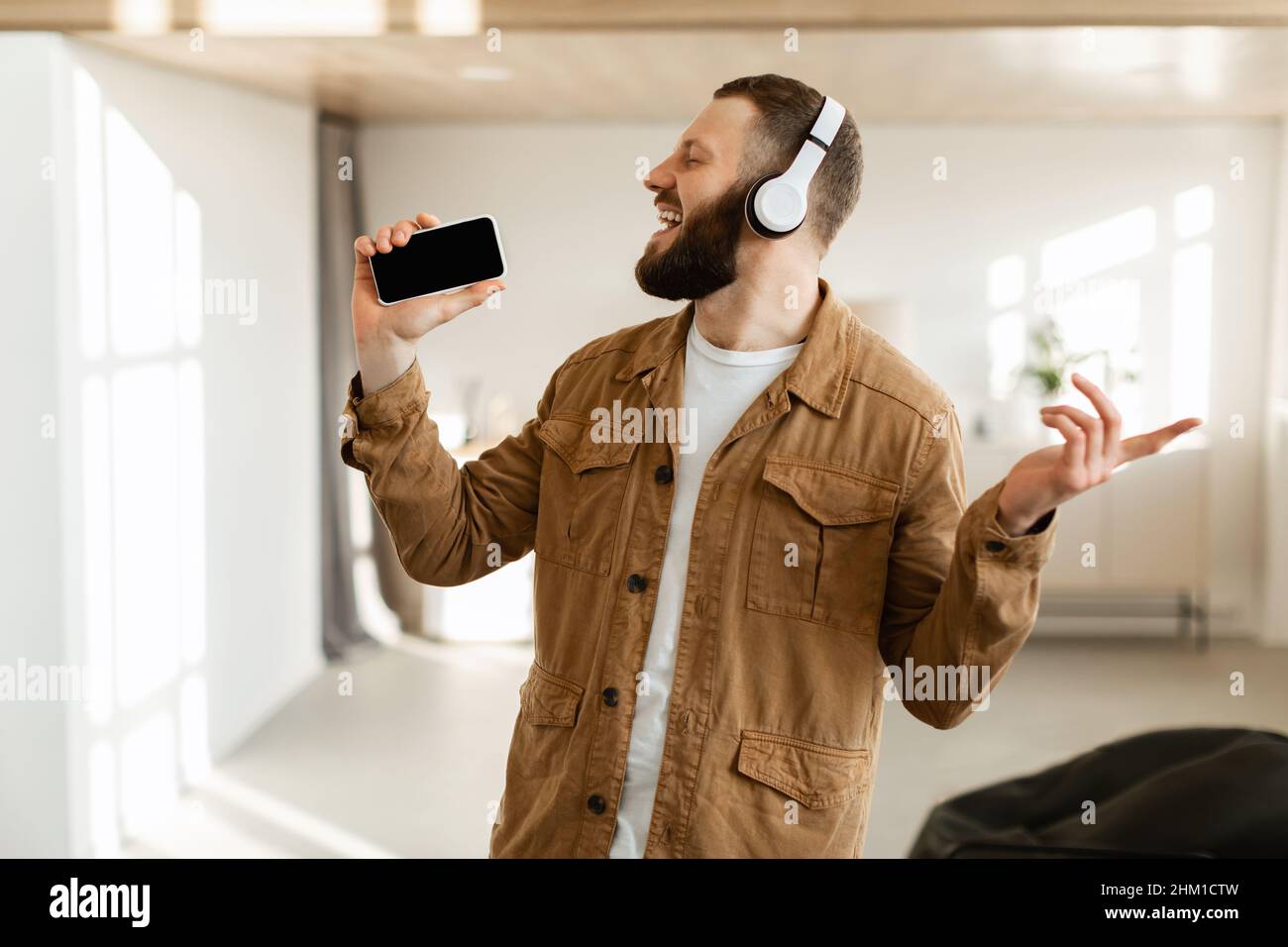 Uomo che ascolta musica sul telefono che urla indossando le cuffie a casa Foto Stock