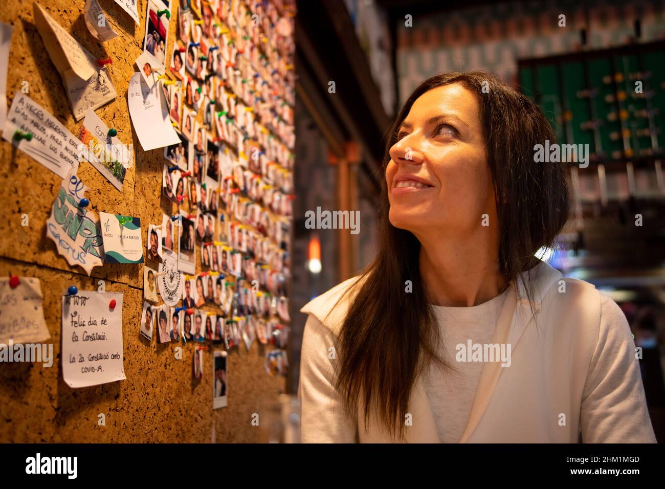 Giovane donna seduta in un bar che guarda un muro con annotazioni e foto del passaporto Foto Stock