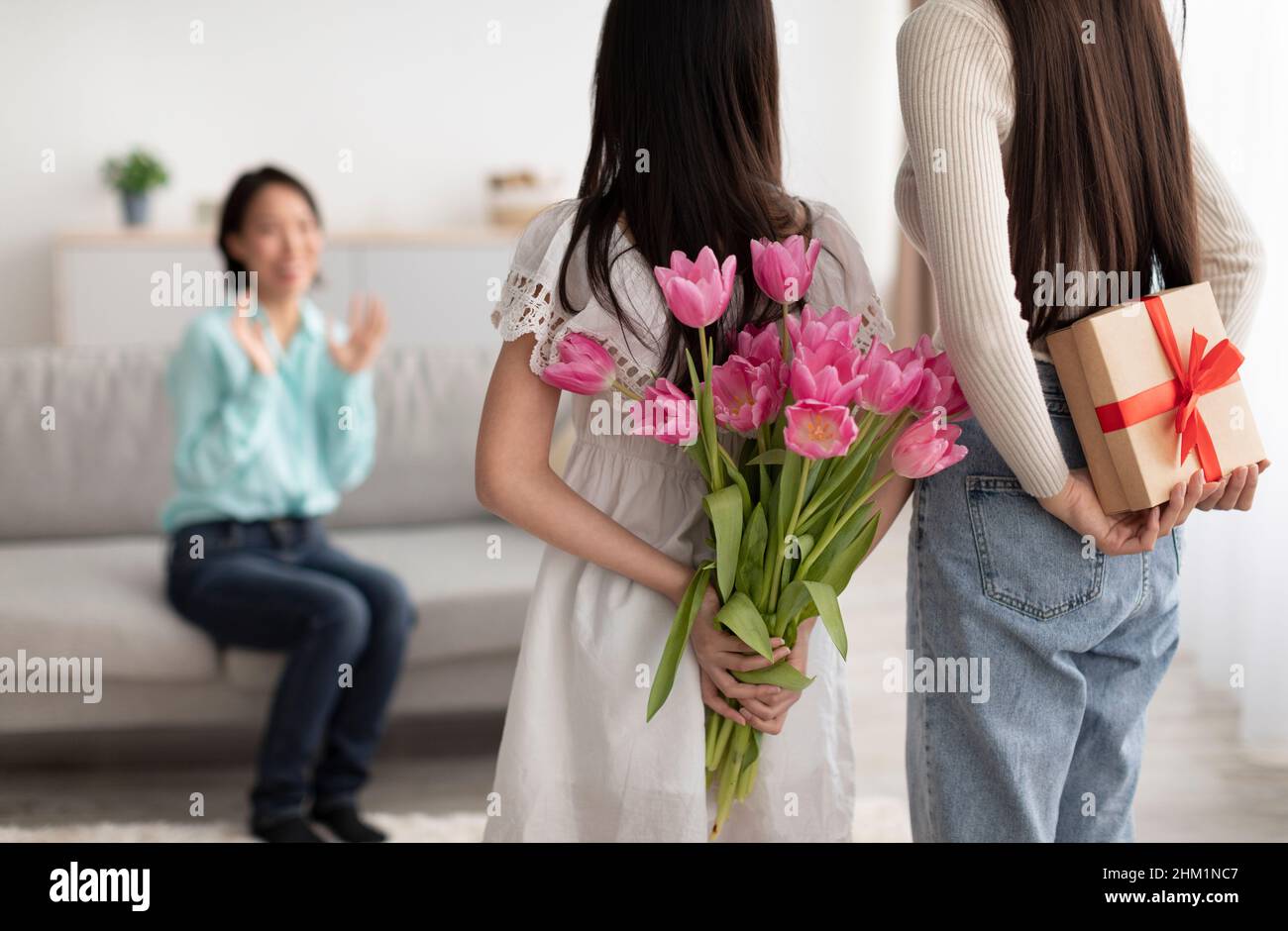 Ragazza asiatica con tulipani mummy nascondere e scatola regalo per donna anziana dietro le loro spalle, salutarla con la festa di primavera a casa Foto Stock