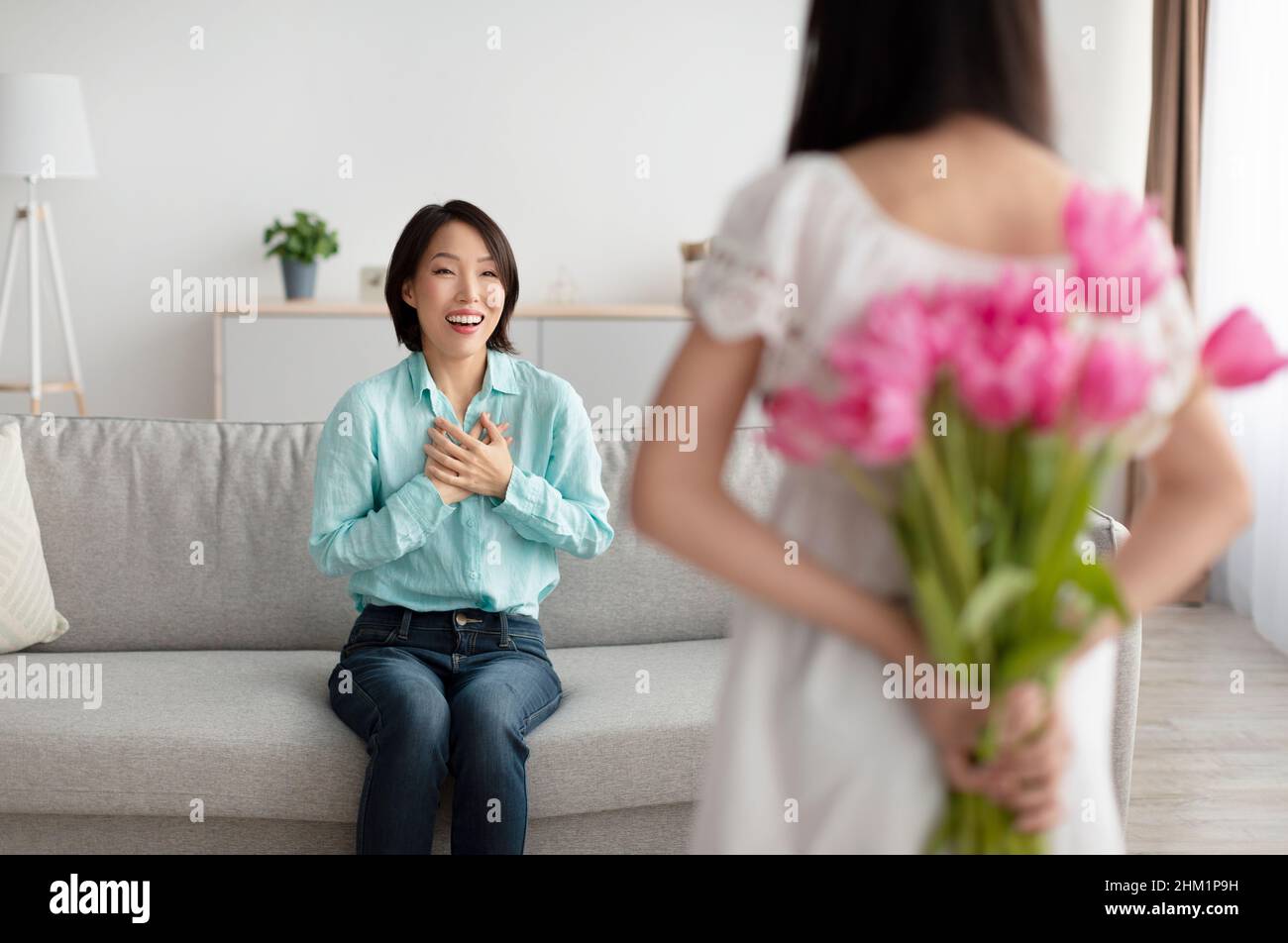 Bambina che tiene bouquet di tulipani per felice asiatico nonna dietro la schiena, rendendo la vacanza sorpresa a casa Foto Stock
