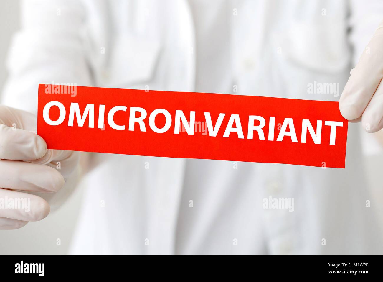 Simbolo di avvertimento rosso con scritta nella variante Omicron. Nuova variante Omicron covid 19 in mani mediche in camice bianco e guanti. Foto Stock