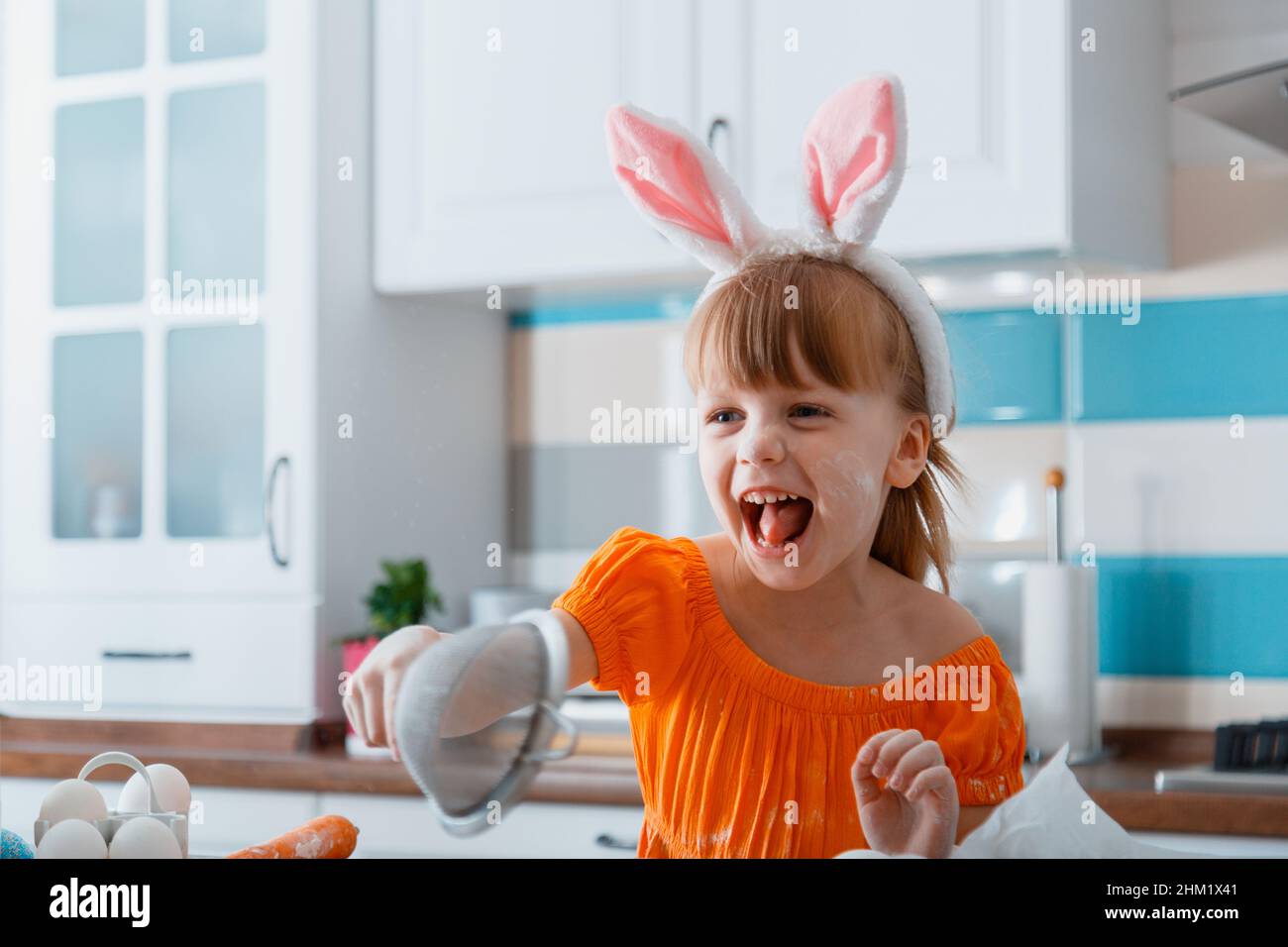 Ritratto emozionale di ragazza allegra vestita come coniglietto per Pasqua mentre cucinano cibo in cucina a casa. Ragazza bambino che ha divertimento ride gioca Foto Stock