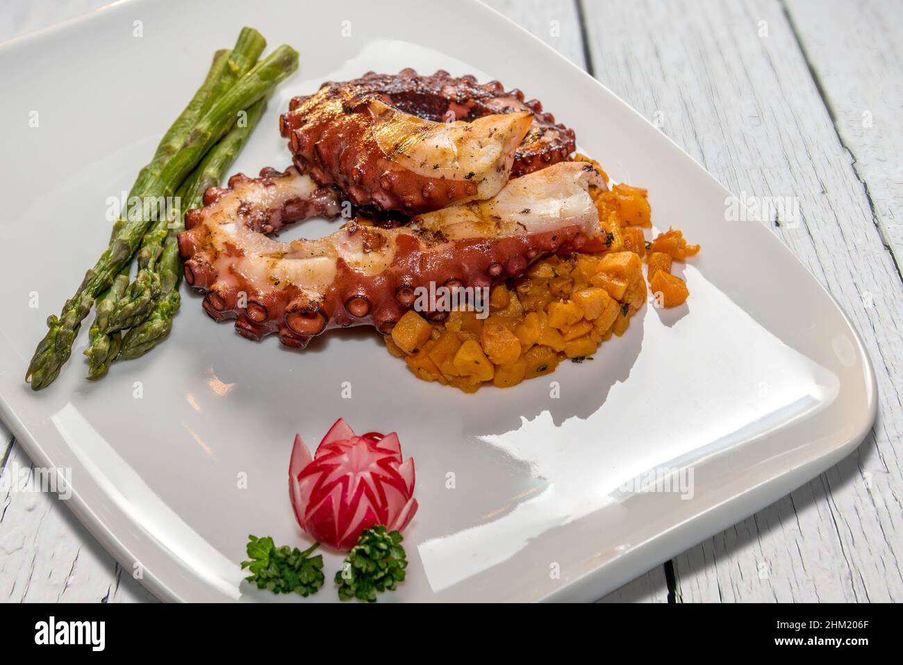 Tentacoli di polpo arrosto con carote e asparagi in piatto bianco su tavole di legno bianco Foto Stock