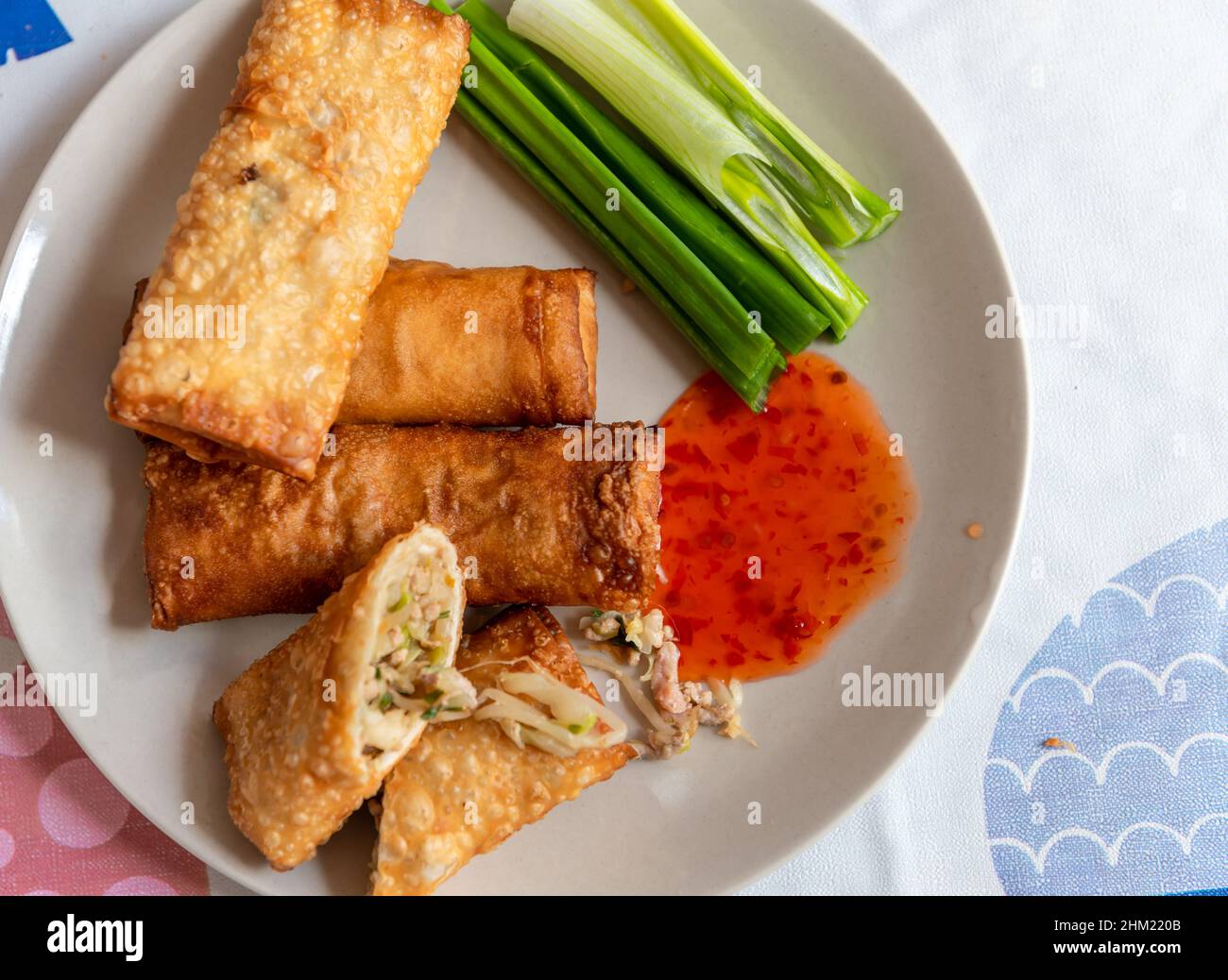 Involtini primavera fritti interi e tagliati serviti su un piatto con cipolle verdi e salsa di peperoncino dolce tailandese. Foto Stock