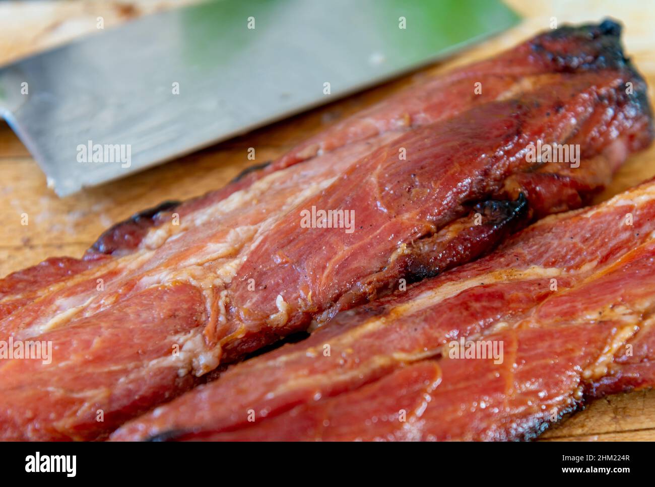 Primo piano di pezzi interi di maiale arrosto al miele cinese su un asse di legno pronto per essere tagliato per servire. Foto Stock