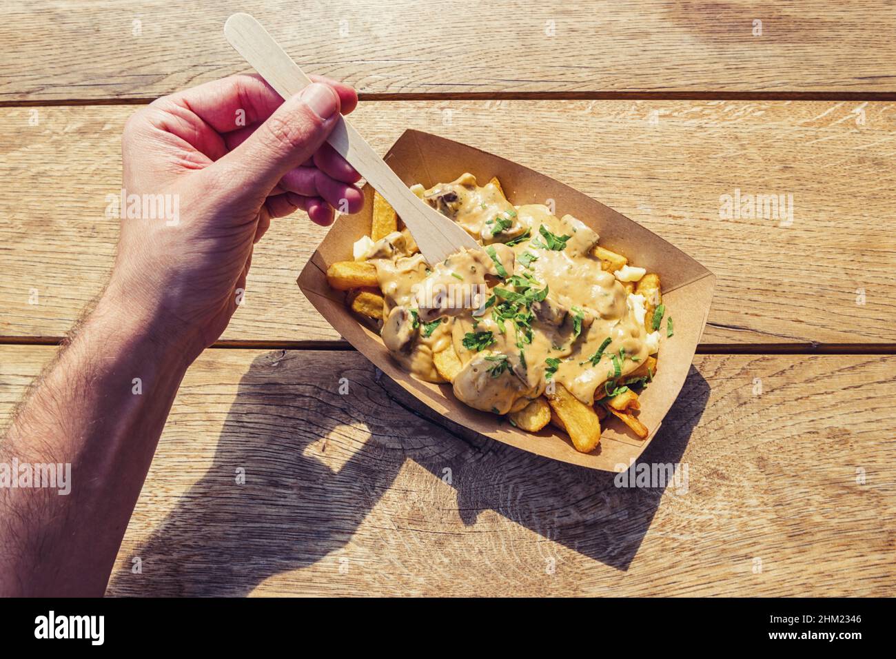 Uomo tenere una forchetta per mangiare patatine fritte con salsa di funghi su un tavolo di legno, punto di vista shot. Foto Stock