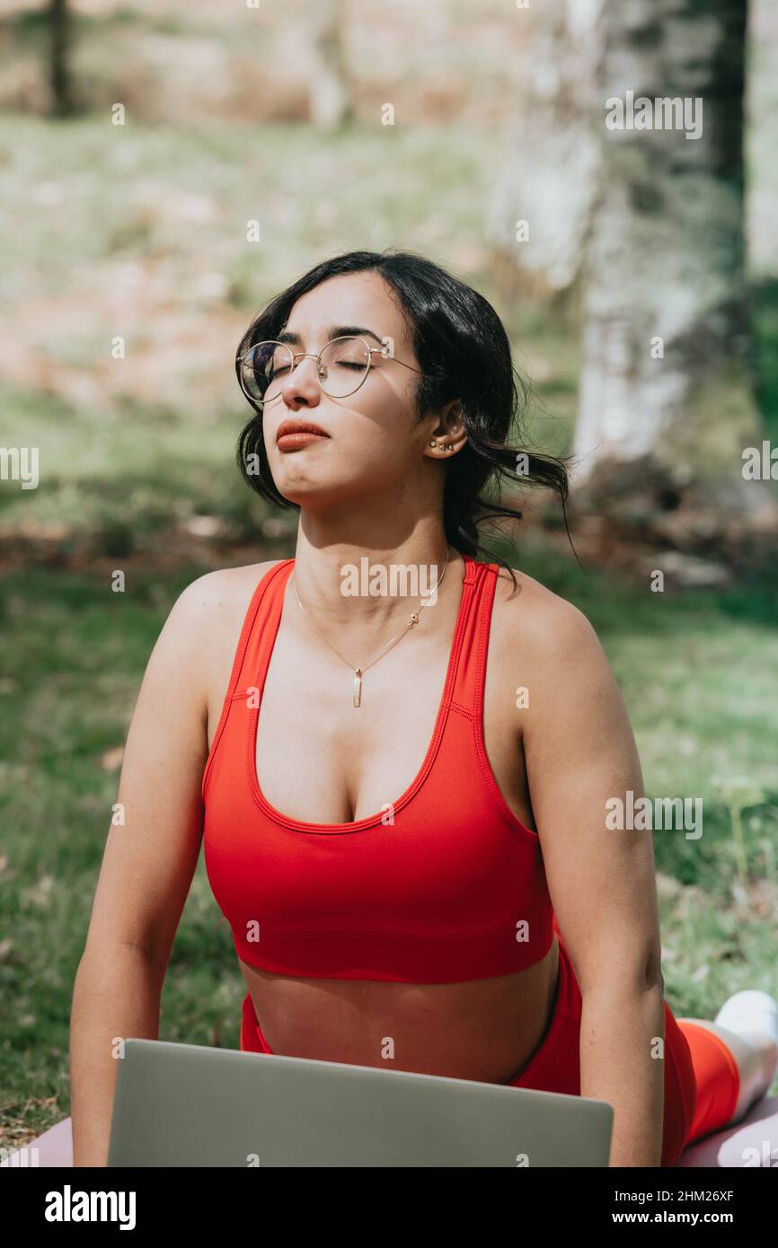 Giovane donna in abbigliamento fitness che fa un esercizio di yoga mentre chiude gli occhi rilassarsi al parco Foto Stock