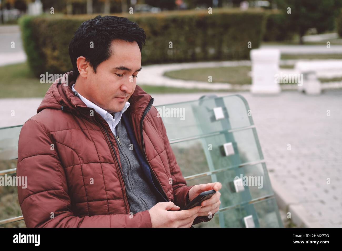 Uomo asiatico di mezza età seduto sul banco con telefono. Foto Stock