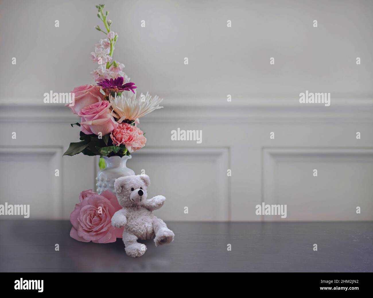 Un orsacchiotto bianco appoggiato a un bouquet di fiori su un tavolo Foto Stock