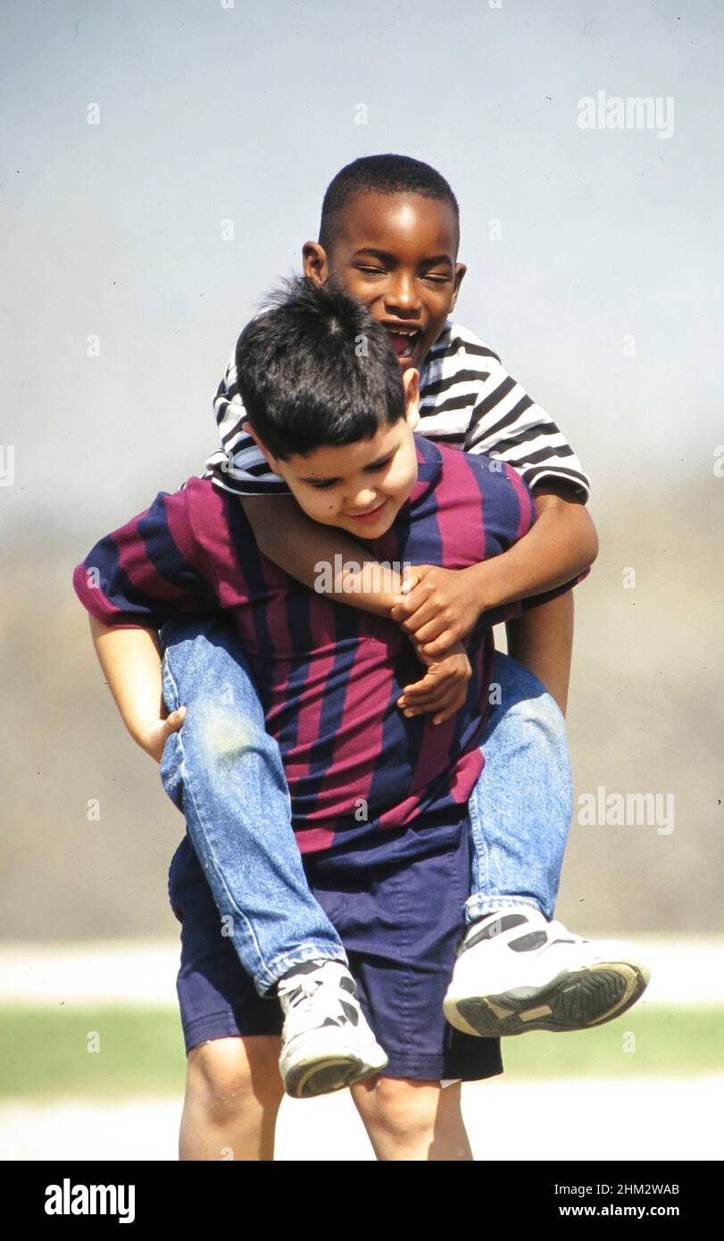 Austin Texas USA, 1989: Il ragazzo ispanico dà al ragazzo nero un giro di piggy-back durante il recesso della scuola elementare. ©Bob Daemmrich Foto Stock