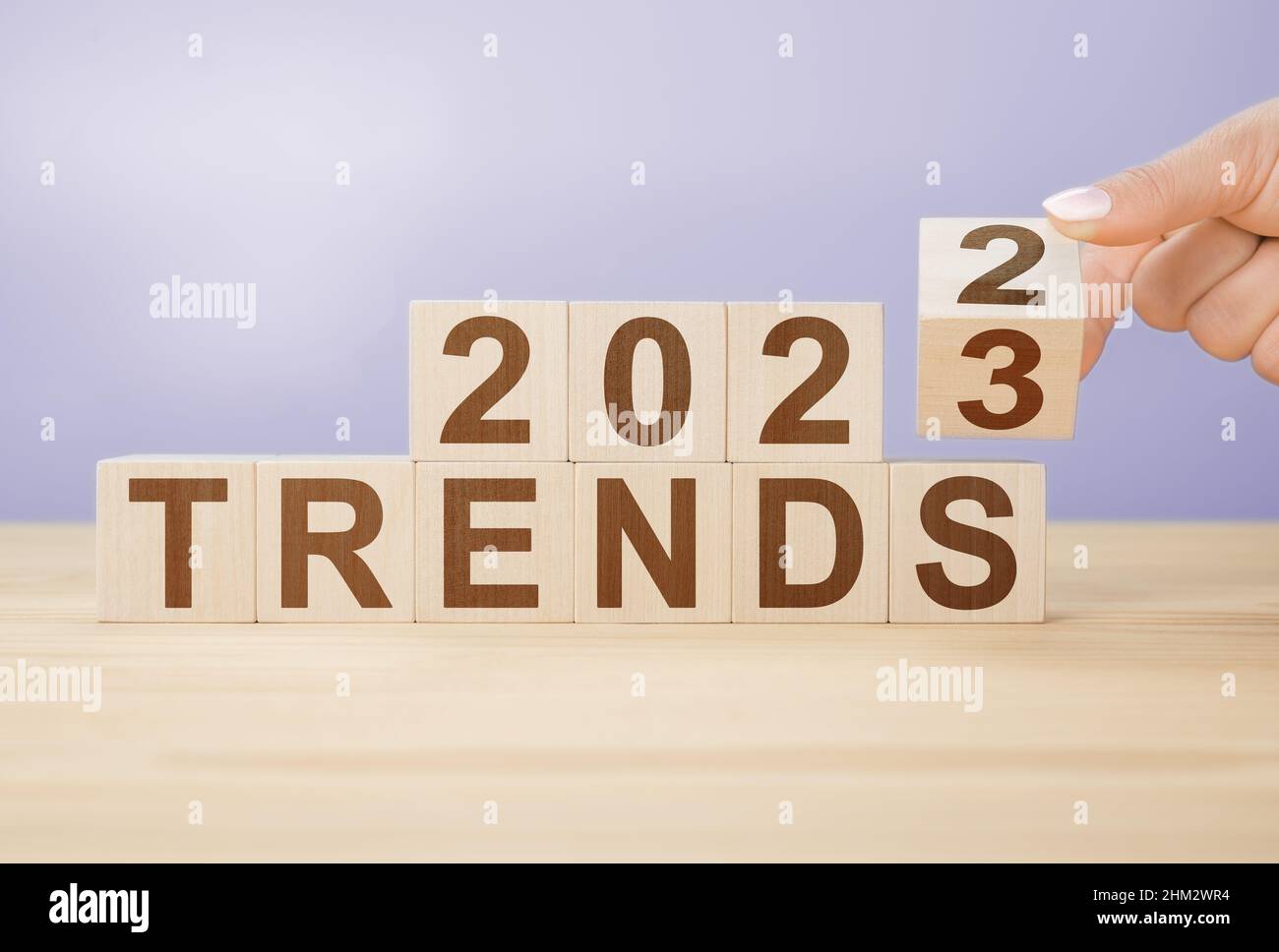 Businesswoman trasforma il cubo di legno e cambia le parole 2022 a 20223 su uno sfondo di colore molto peri. Flipping di blocco di cubo di legno per il cambiamento da 2022 a 2023 y Foto Stock