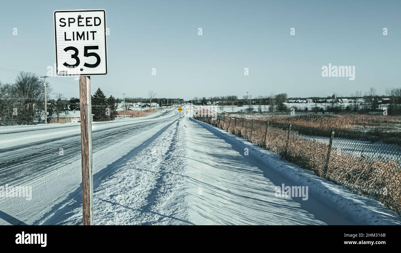 Segnale di velocità con strade coperte di neve e marciapiede.paesaggio ghiacciato si dirige verso l'orizzonte. Foto Stock