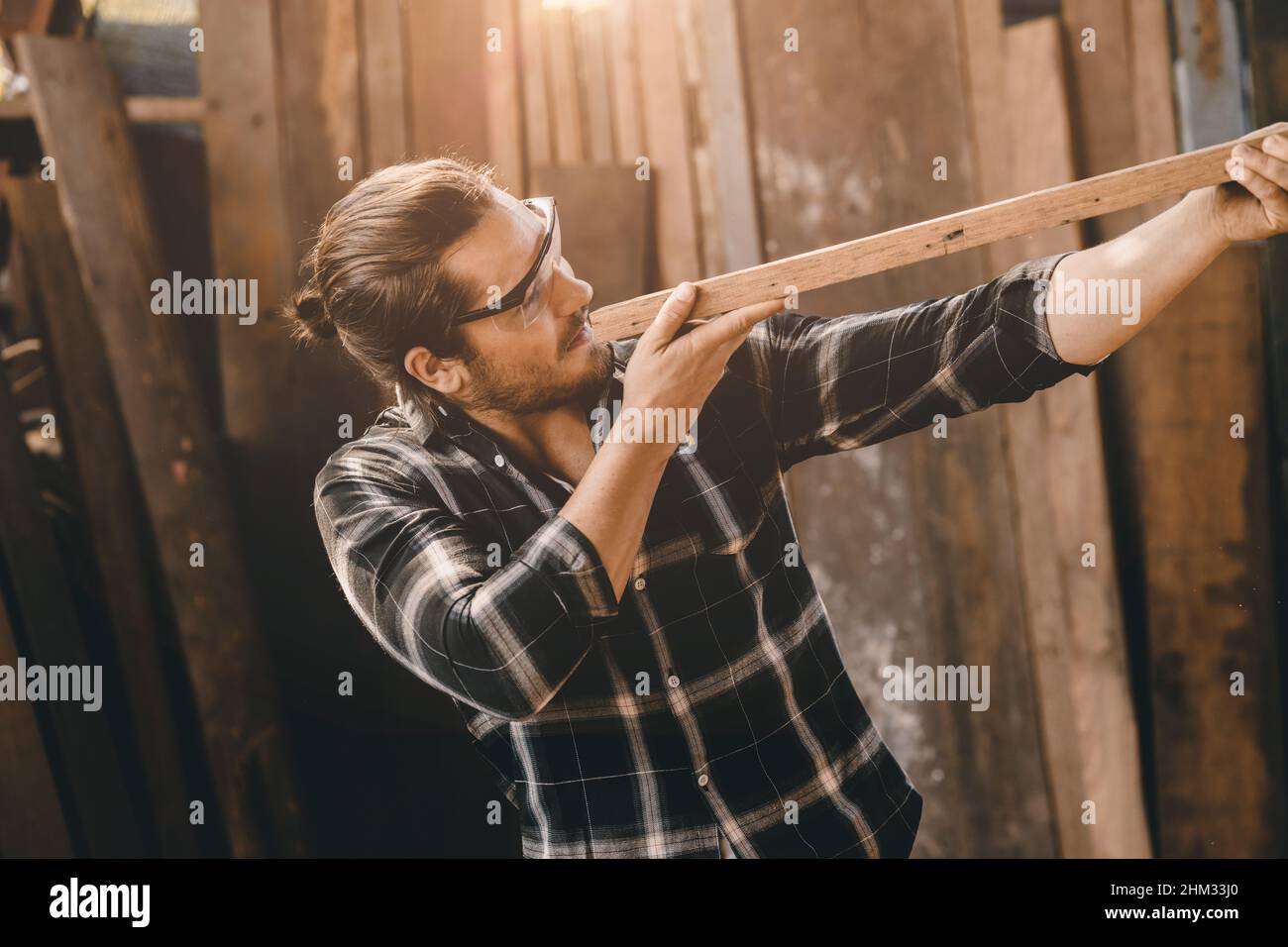 L'uomo carpentieri alto esperto legno che fa mobili. Maestro di legno maschio guardando il pannello di legno. Foto Stock