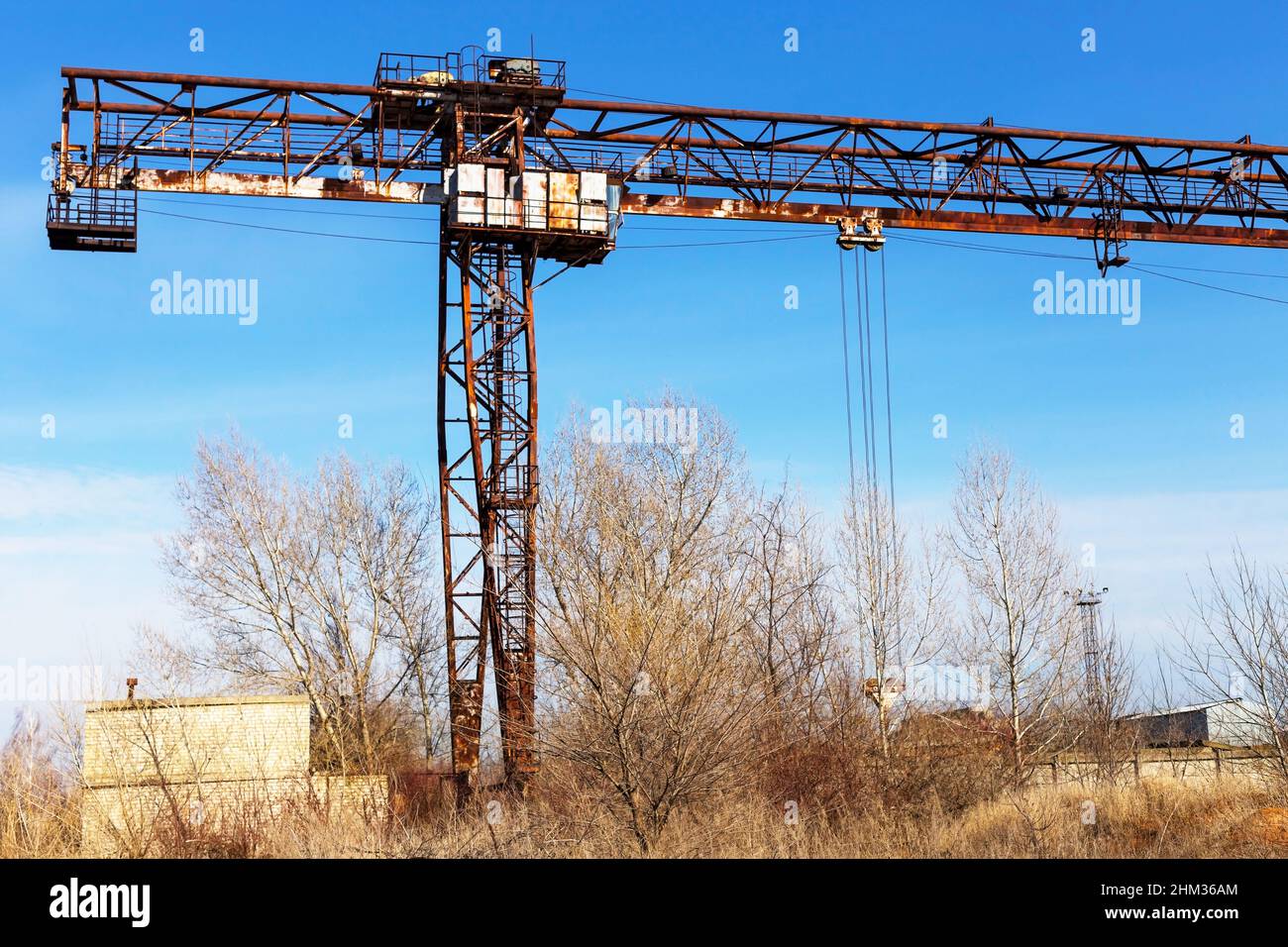 Vecchia gru a portale arrugginita sulla ferrovia, una pianta di cemento abbandonata. La crisi, il crollo dell’economia e la chiusura delle capacità produttive hanno portato al confronto Foto Stock