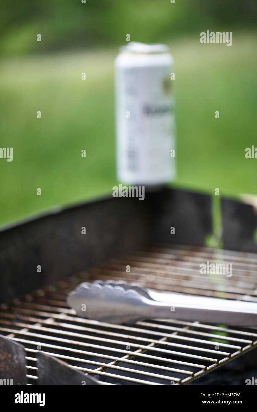 Griglia sporca, barattoli di birra bianca e pinze per grigliate in acciaio inox. Natura verde sullo sfondo. Vista laterale. Foto Stock