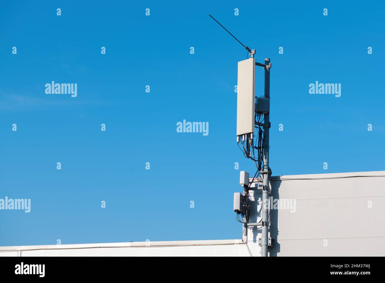 Antenna ripetitore segnale cellulare montata sulla parte superiore dell'edificio industriale con cielo blu come spazio di copia Foto Stock
