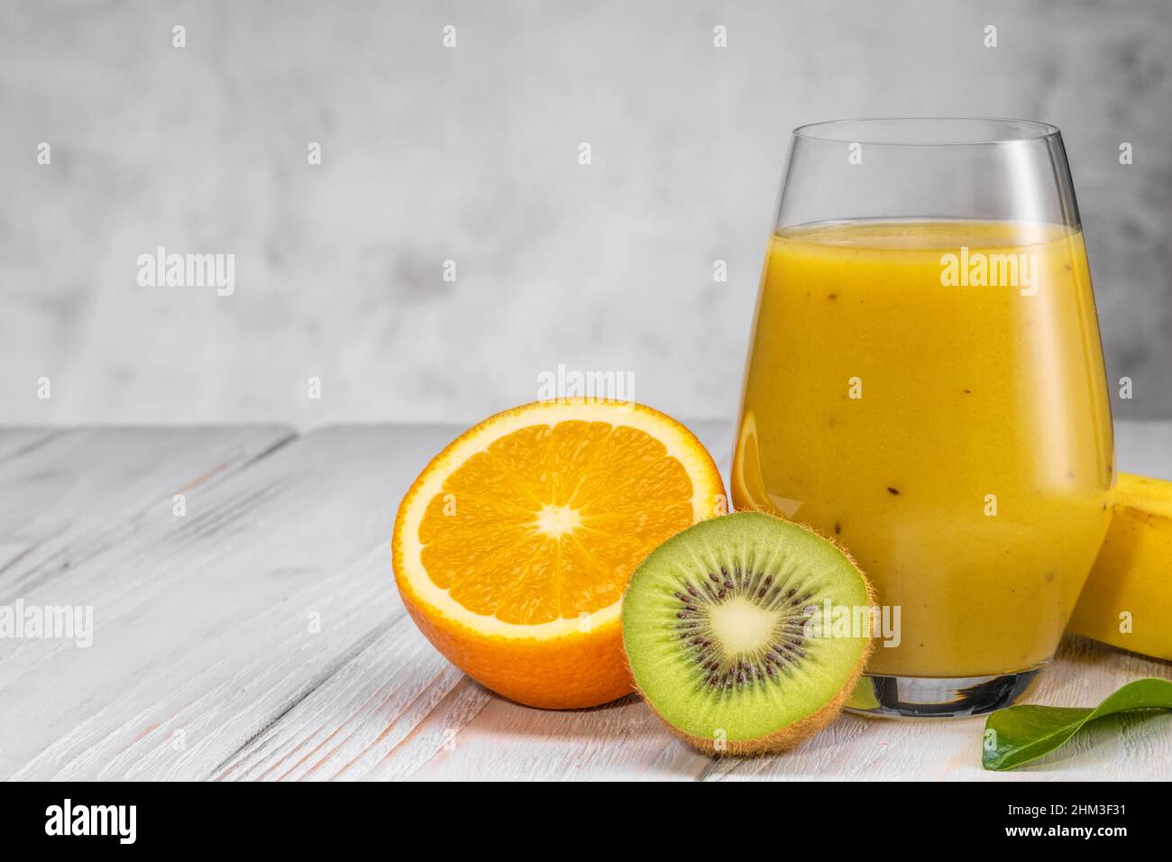 Bicchiere di banana verde, arancia e kiwi sani frullati. Foto Stock