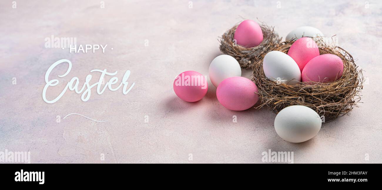 Uova di Pasqua rosa e bianche in un nido e su sfondo rosa chiaro. Il concetto di Buona Pasqua. Vista laterale. Foto Stock