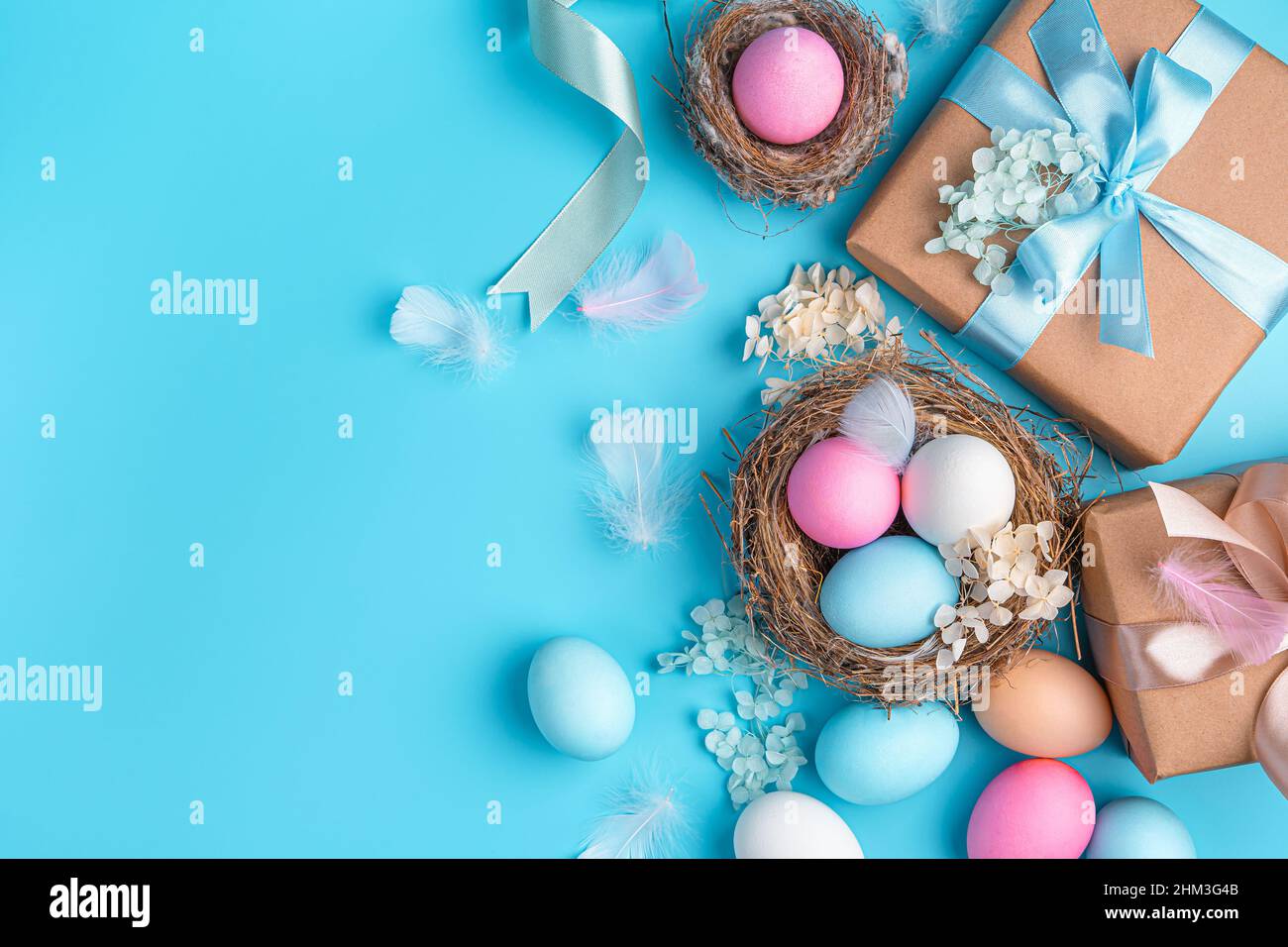 Sfondo pasquale con uova colorate, nidi e regali su sfondo blu. Buona Pasqua. Vista dall'alto, spazio di copia. Foto Stock