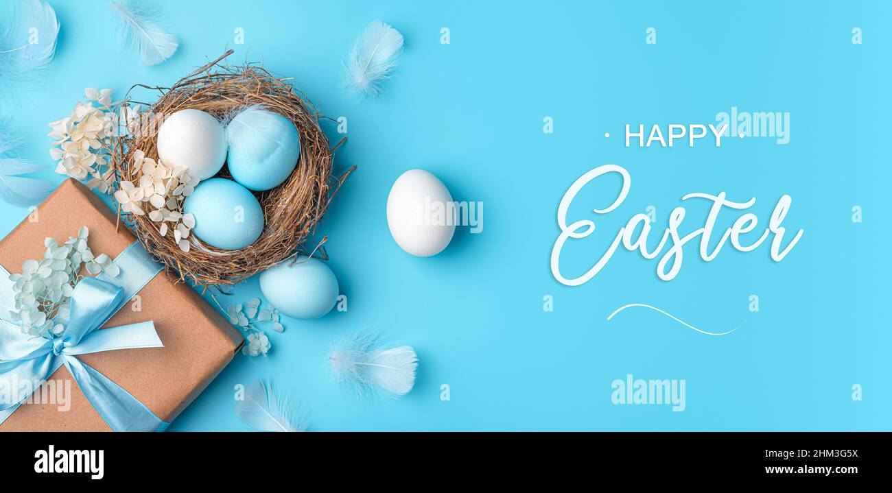 Un nido con uova di Pasqua, un regalo e piume su sfondo blu. Il concetto di Buona Pasqua. Vista dall'alto. Foto Stock