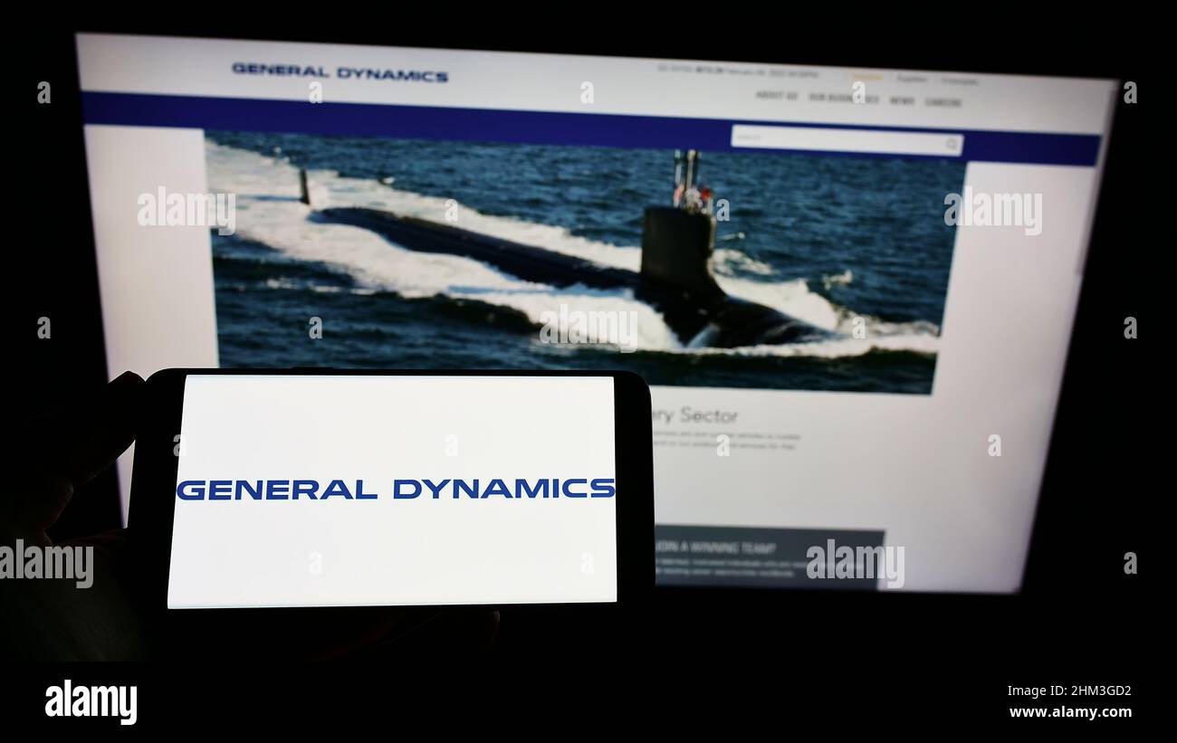 Persona che tiene uno smartphone con il logo della società statunitense General Dynamics Corporation (GD) sullo schermo di fronte al sito Web. Mettere a fuoco sul display del telefono. Foto Stock