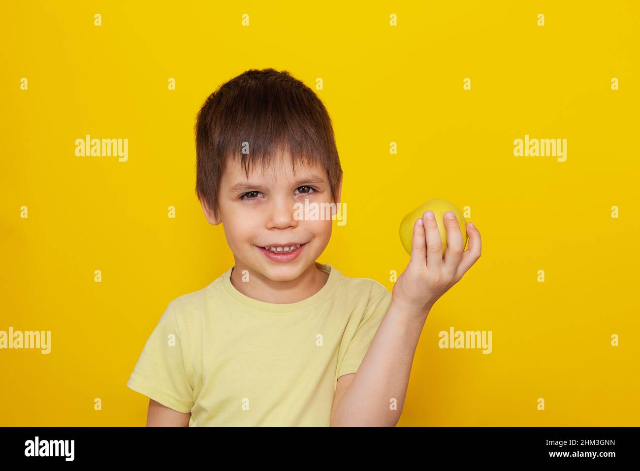 Un bambino allegro in una T-shirt gialla su sfondo giallo tiene una mela nelle sue mani. Il concetto di cibo sano per i bambini. Spazio di copia Foto Stock